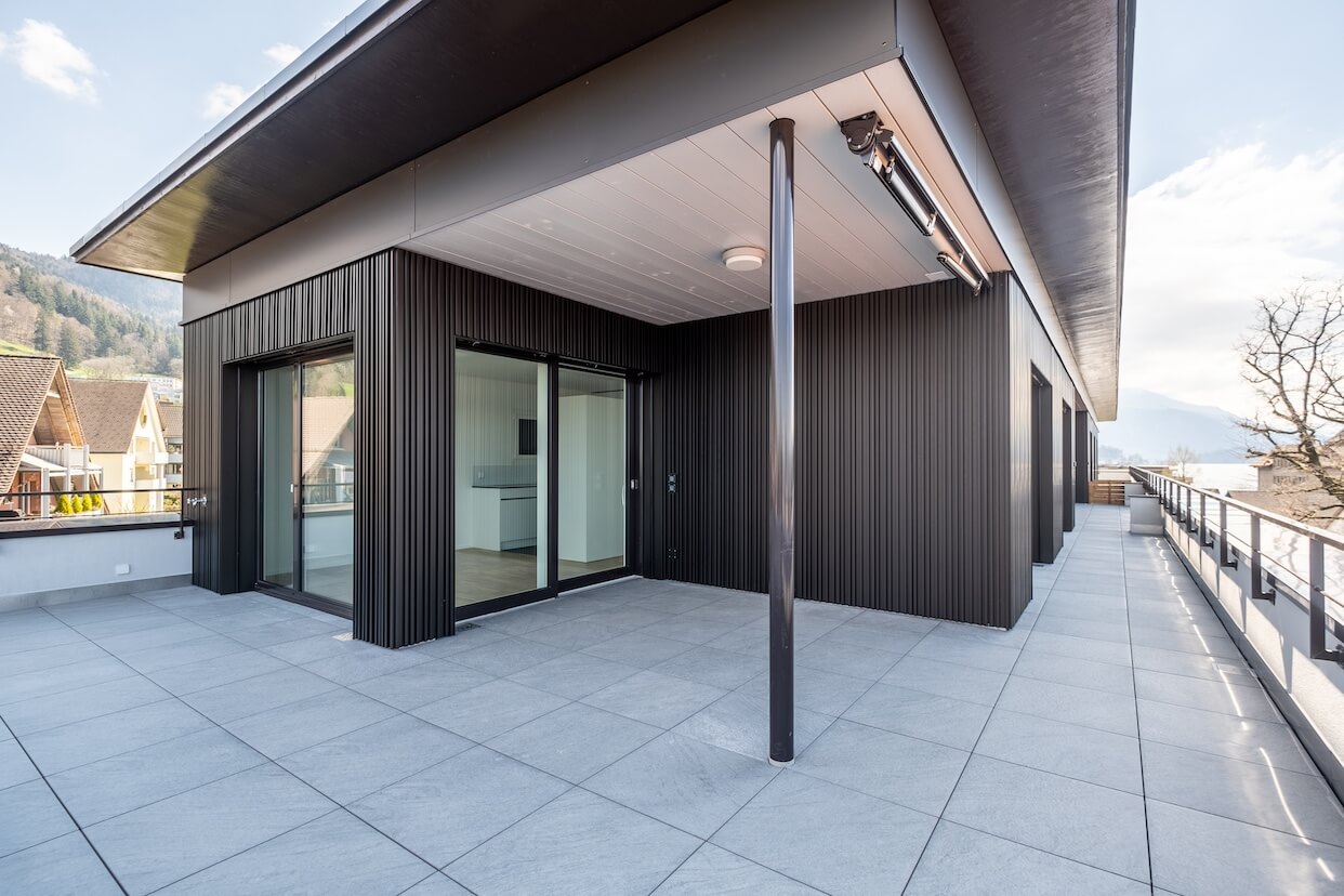 Moderne Terrassenfassade mit dunklen Metallpaneelen und grosszügiger Verglasung mit Blick auf die Berge.